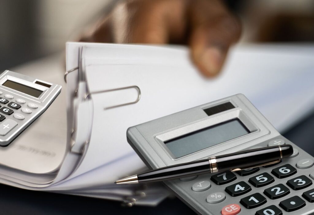 A calculator and pen placed over a stack of papers, representing financial planning and calculations.