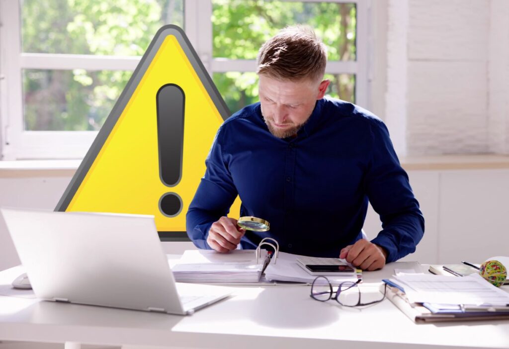 A person closely examining documents with a magnifying glass, symbolising caution and awareness of financial scams.