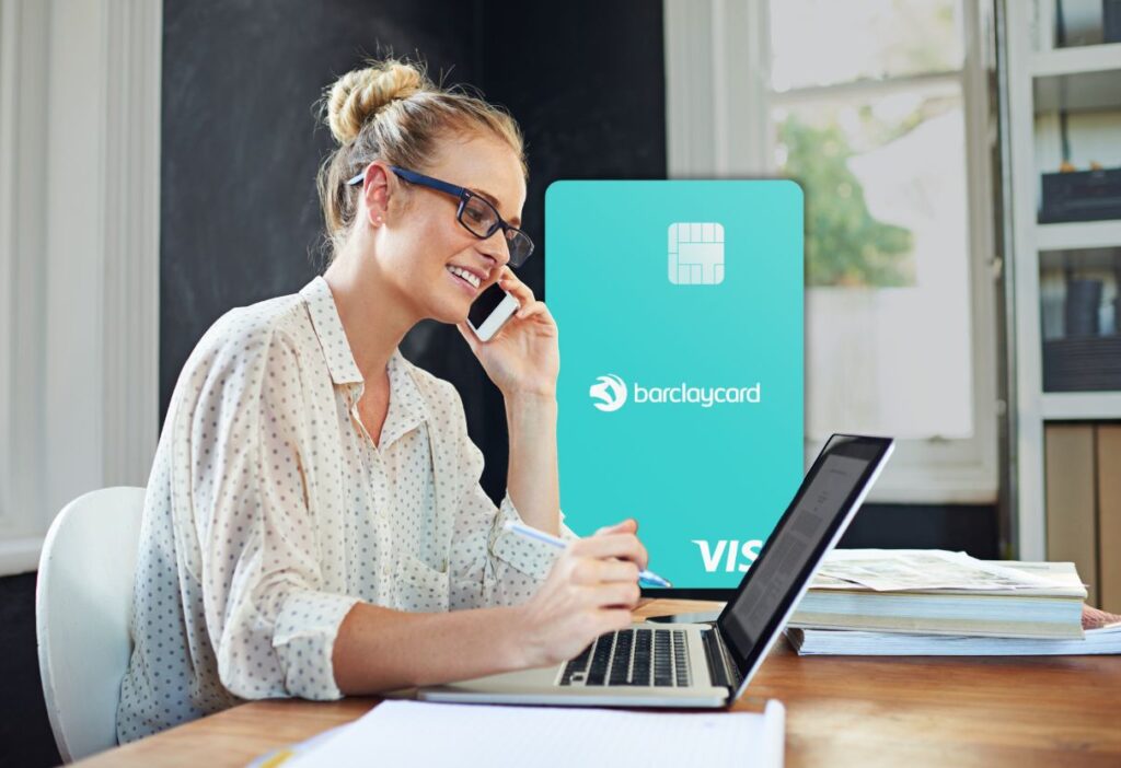 Woman with glasses and blonde hair tied up, sitting at a desk, talking on the phone while working on a laptop. In the foreground, a turquoise Barclaycard Forward Visa credit card is displayed.