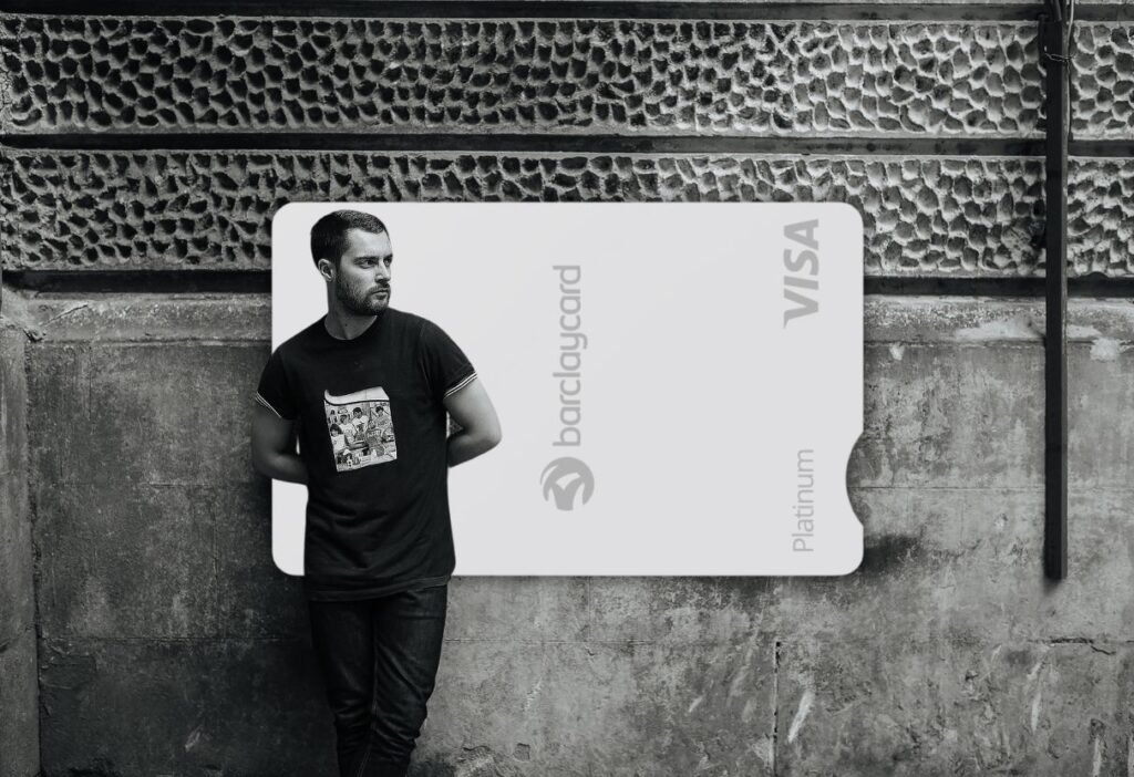 A man in a casual outfit leans against a textured concrete wall with a Barclaycard Platinum Balance Transfer Card prominently displayed in the background.