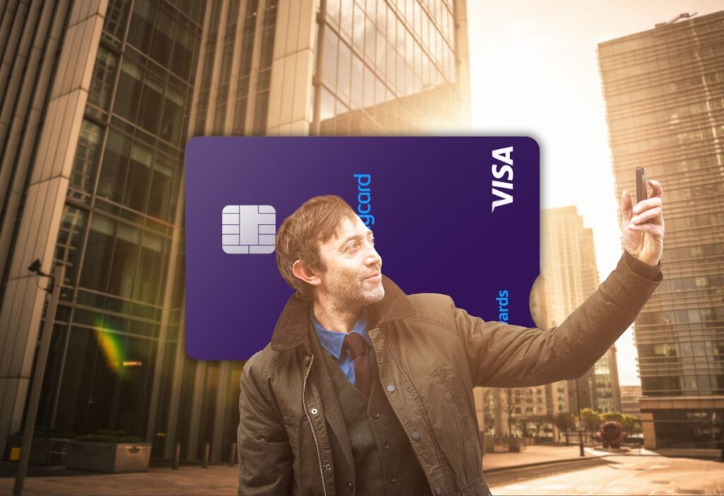 A man taking a selfie in a modern cityscape, with the Barclaycard Rewards Credit Card in focus, highlighting travel and everyday spending benefits.