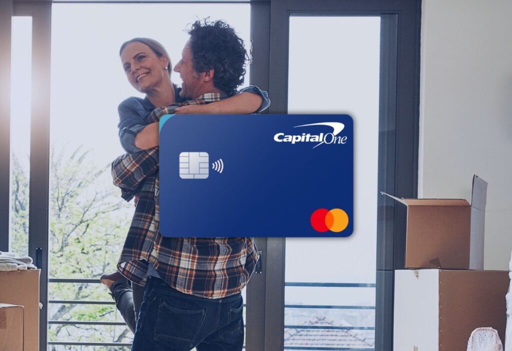 Joyful couple embracing in their new home with a blue Capital One credit card overlay, highlighting the financial freedom for life’s major milestones.