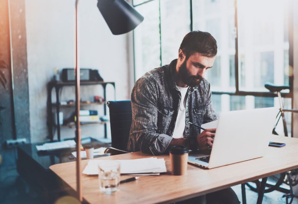 A man working on a laptop at a desk in a modern office, symbolising focus and research.