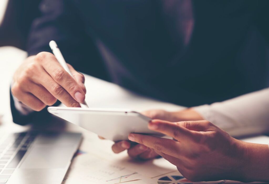 Close-up of hands using a stylus on a tablet, representing financial analysis and digital research.