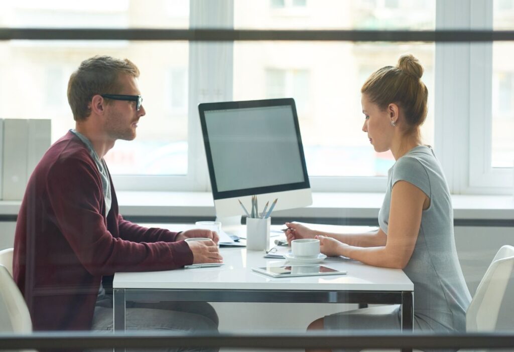 Two professionals sitting across a desk from each other, engaged in a discussion, suggesting a financial advisory meeting.