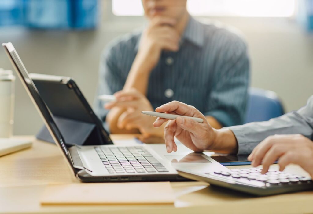 Close-up of hands using a laptop and calculator, indicating a focus on financial calculations and planning.