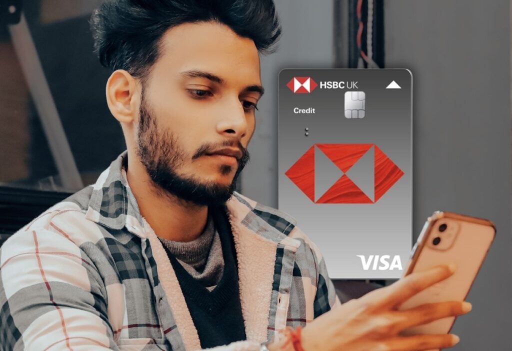 Man holding a smartphone with the HSBC Classic Credit Card visible in the background, showcasing the card’s design with the HSBC logo and Visa branding.