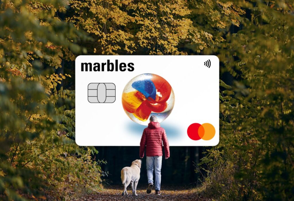 Marbles Credit Card displayed alongside a person walking a dog in an autumn forest, symbolising financial confidence and security.