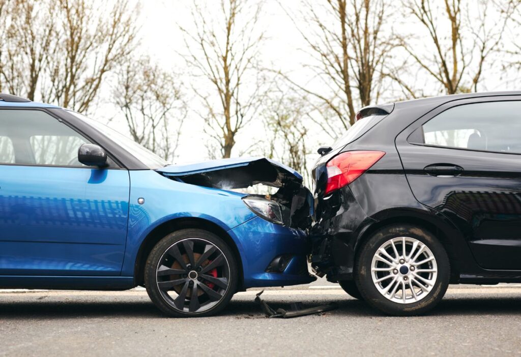 A blue car with a damaged front bumper after a collision with a black car, illustrating car accident risks and the importance of car insurance in the UK.