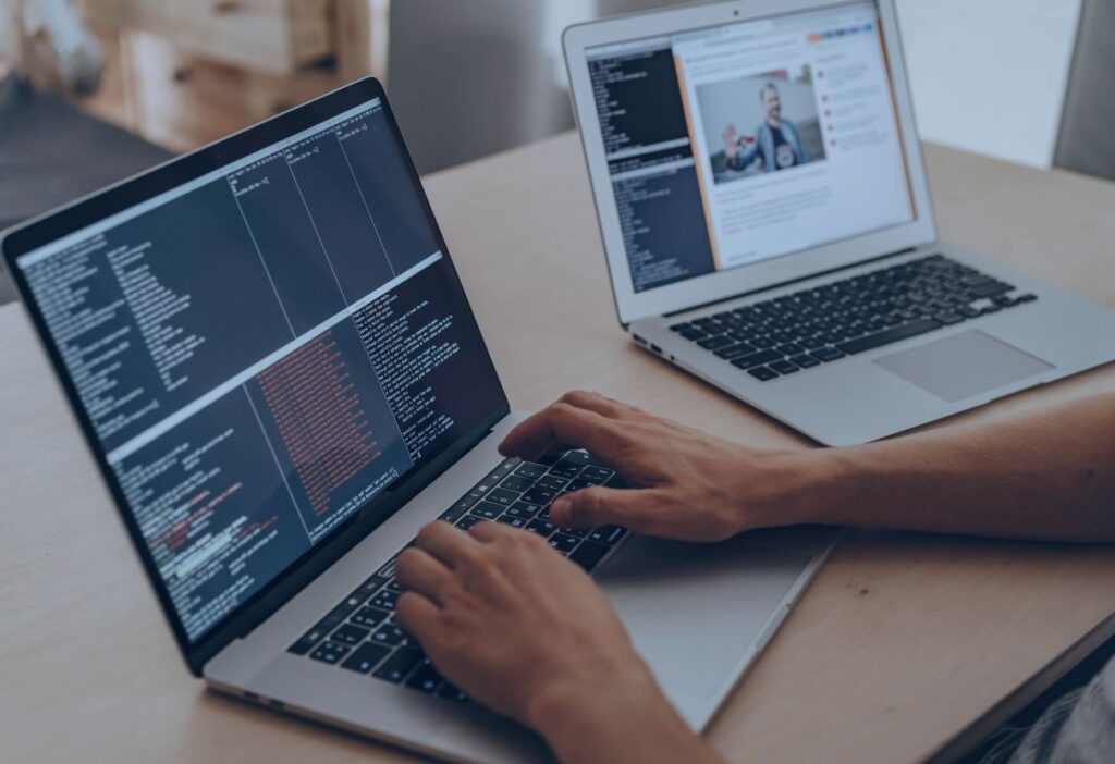 Person typing code on a laptop, with lines of programming text on the screen, symbolising the importance of data security in avoiding financial scams.